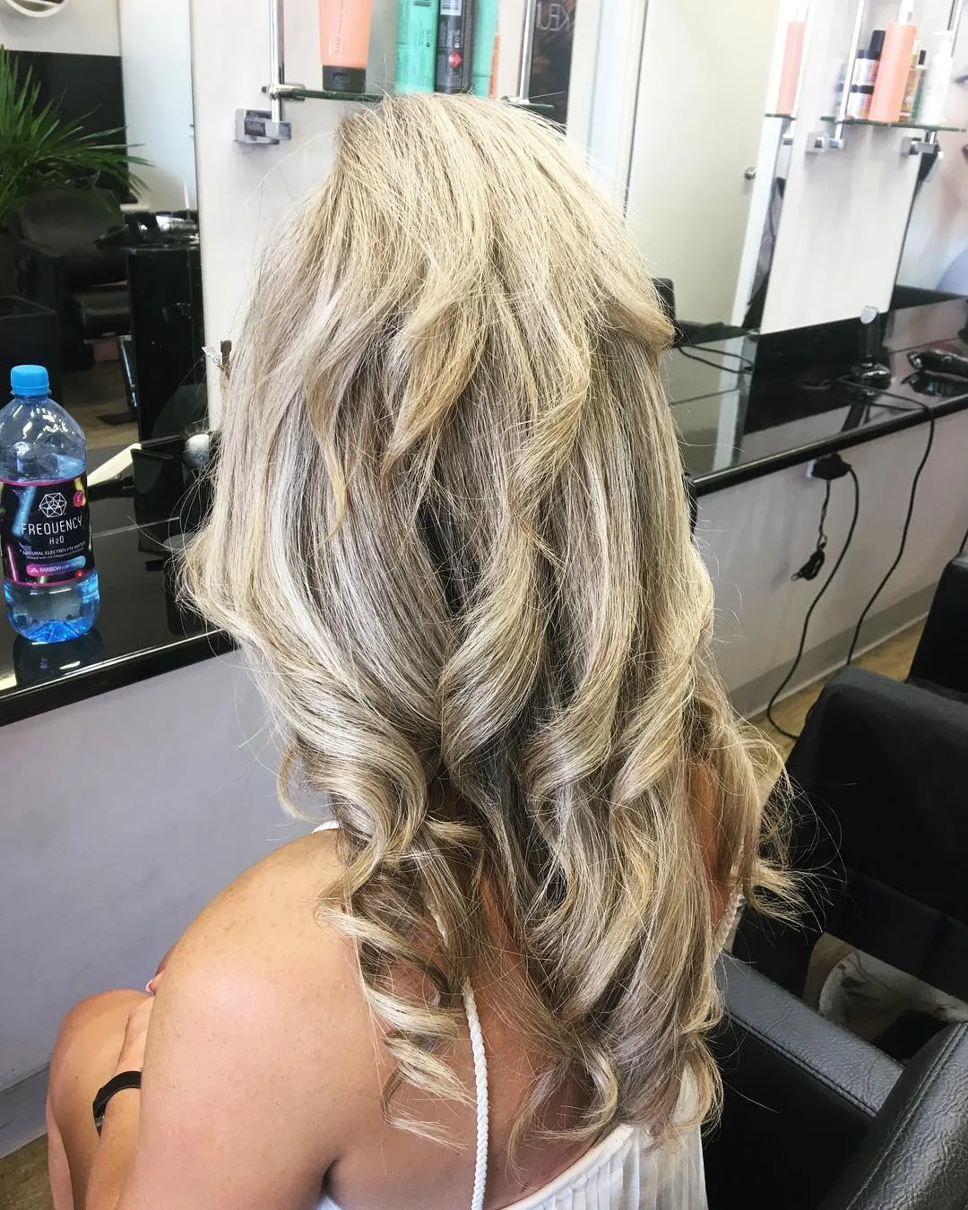Dimensional blonde beach waves with highlights, side-back view at styling station — colour by Jolin