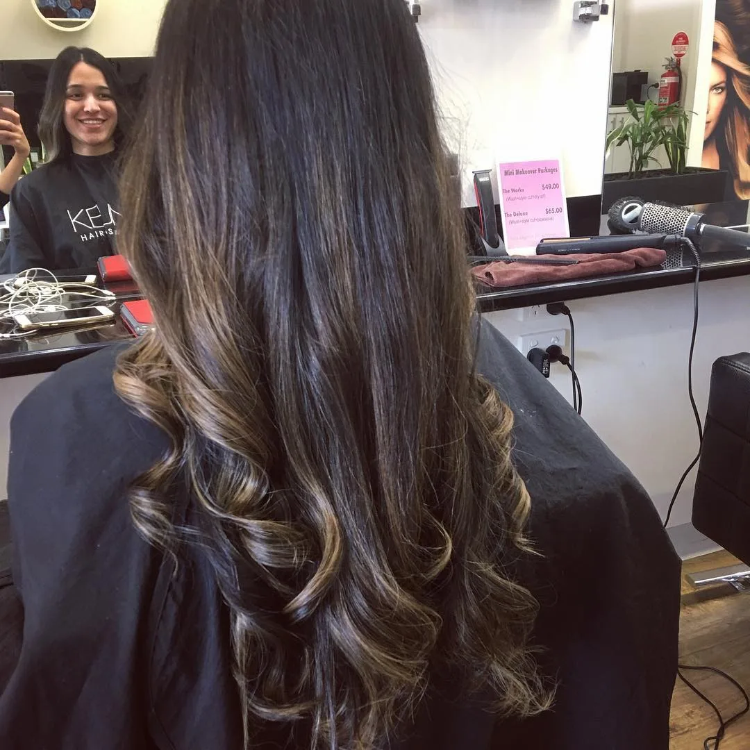Brunette balayage curls, back view at mirror, salon styling counter behind — colour by Jolin